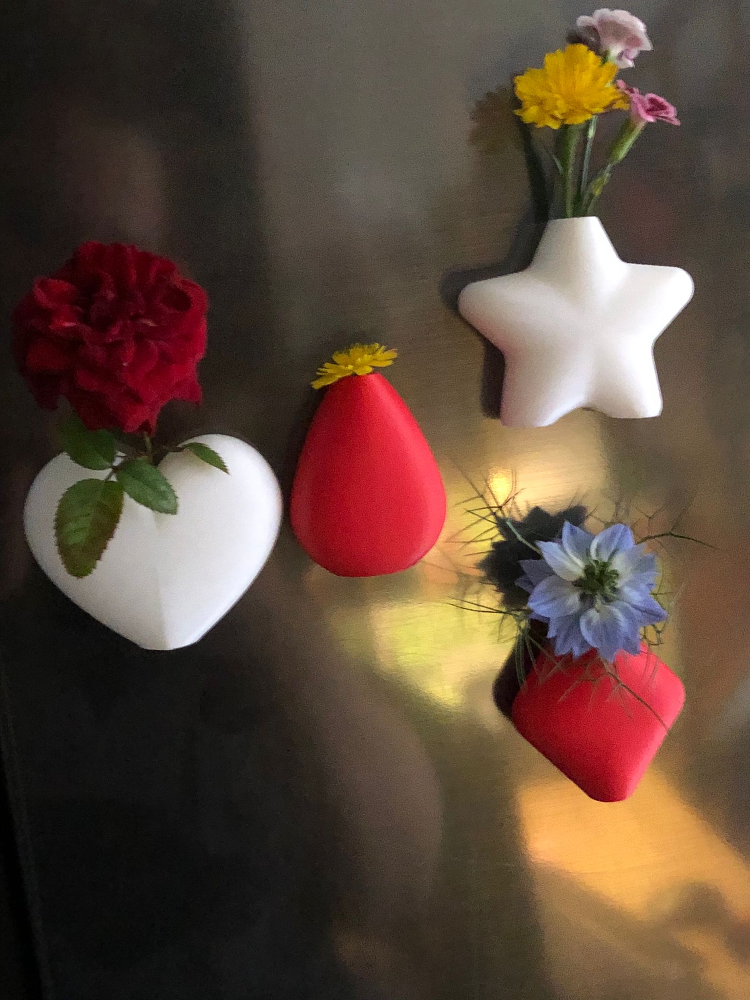 Set of mini magnetic vases in heart, star, diamond, and teardrop shapes, attached to a refrigerator and holding small colorful flowers, displayed in red and white colors.