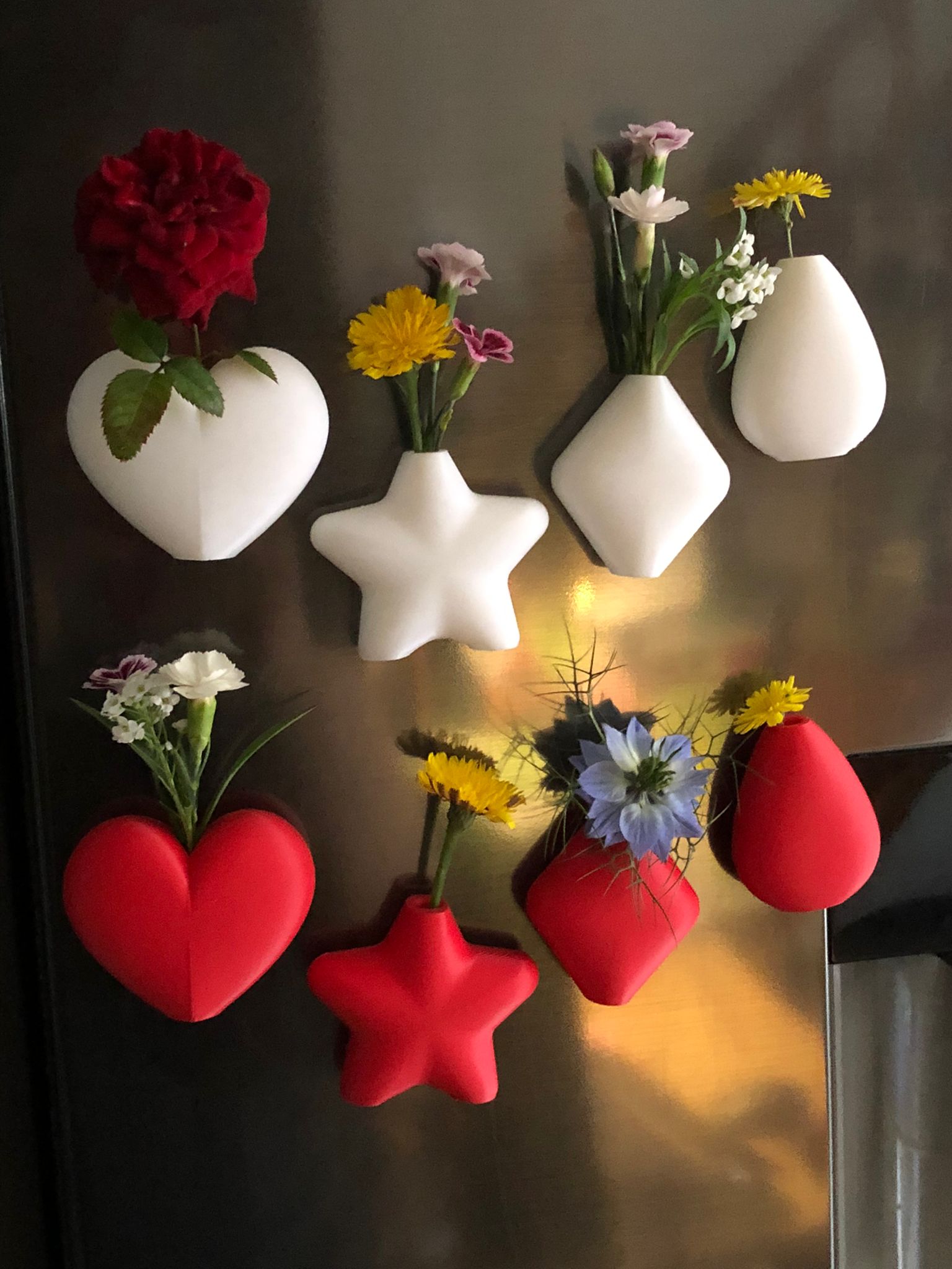 Set of mini magnetic vases in heart, star, diamond, and teardrop shapes, attached to a refrigerator and holding small colorful flowers, displayed in red and white colors.