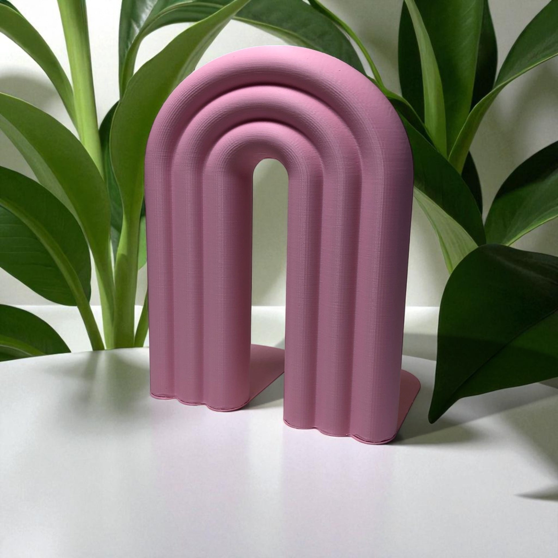 Single-piece rainbow arch bookend in colorful design, displayed on a shelf holding books upright. Ideal for nurseries, kids' rooms, and modern home decor.