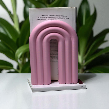 Single-piece rainbow arch bookend in colorful design, displayed on a shelf holding books upright. Ideal for nurseries, kids' rooms, and modern home decor.