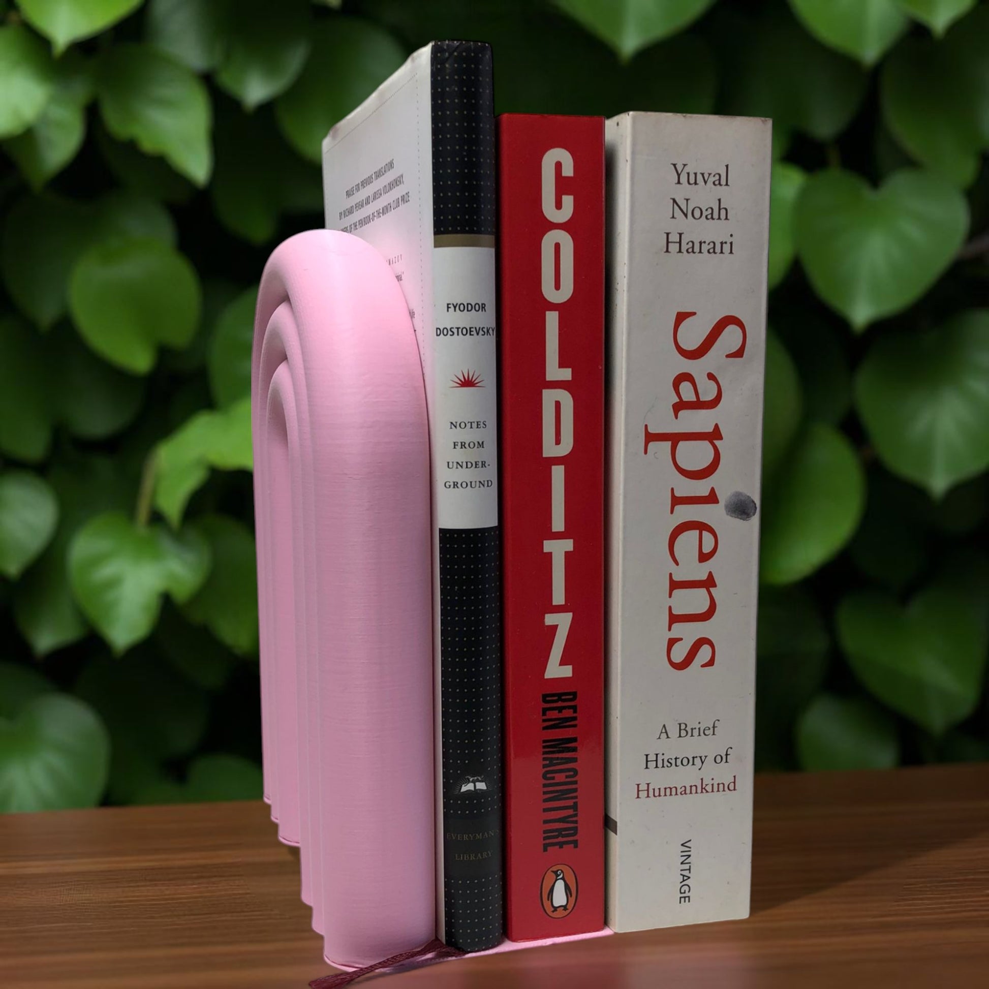 Single-piece rainbow arch bookend in colorful design, displayed on a shelf holding books upright. Ideal for nurseries, kids' rooms, and modern home decor.