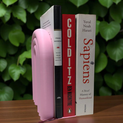 Single-piece rainbow arch bookend in colorful design, displayed on a shelf holding books upright. Ideal for nurseries, kids' rooms, and modern home decor.