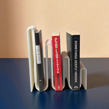 Modern wavy book stand in textured white, holding two books upright; perfect for organizing books, magazines, or vinyls on a desk, shelf, or reading nook
