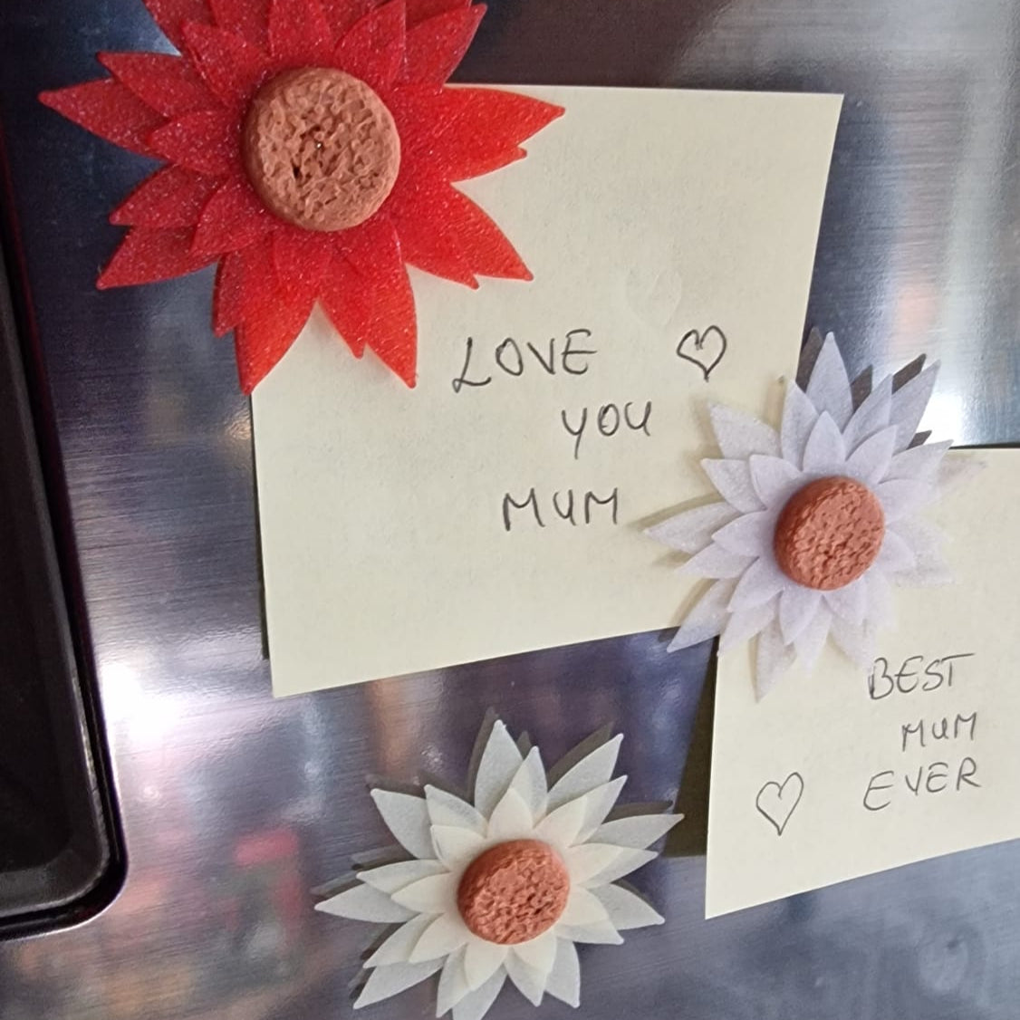 Note with 'Love you Mum' and a red flower magnet on a metallic surface.
