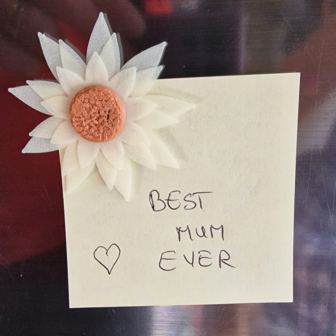 Note with 'Best Mum Ever' and decorative flowers on a reflective surface