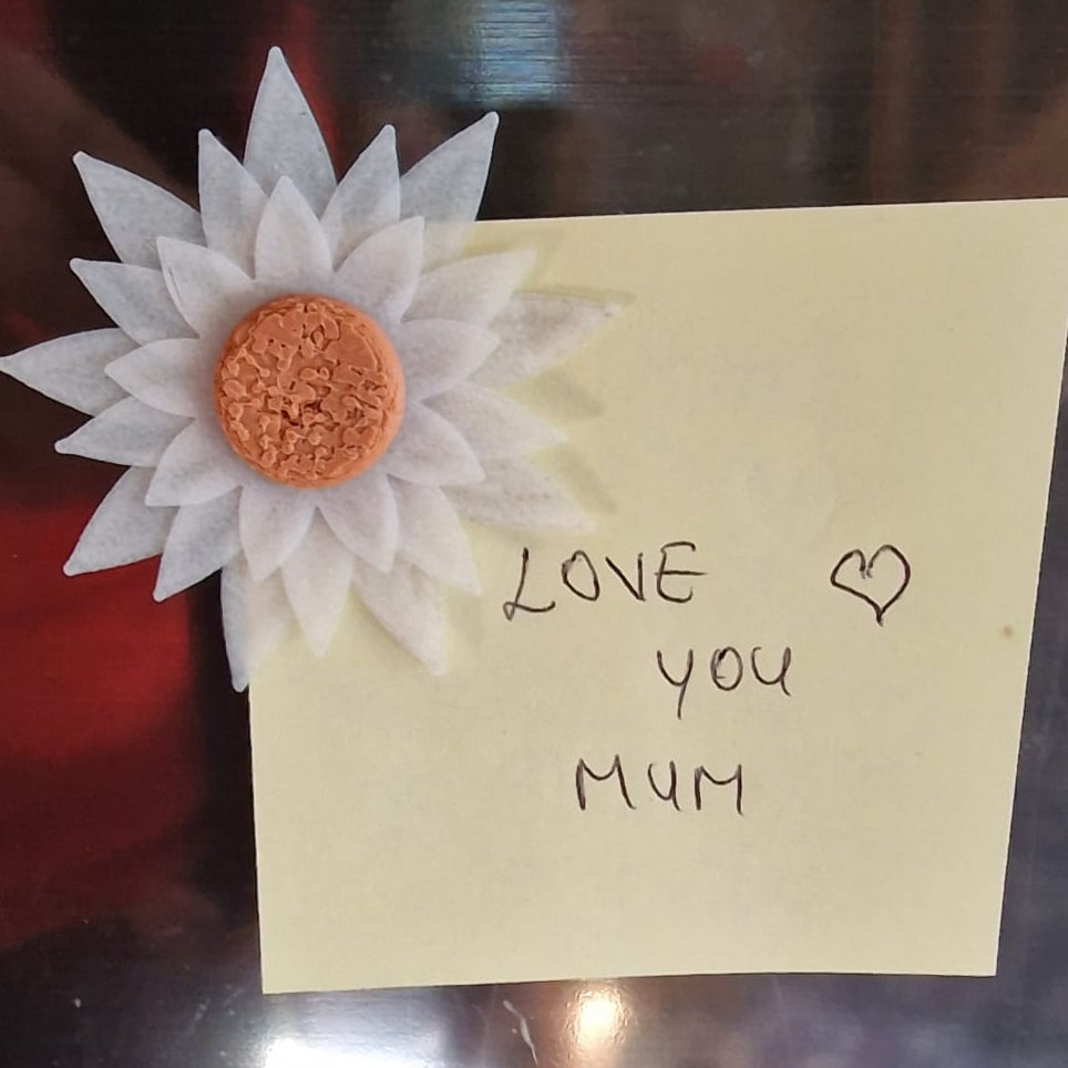 note with 'love you mum' and a flower decoration on a reflective surface.