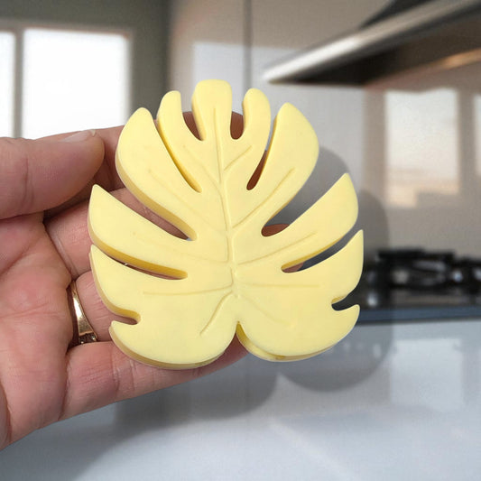 Hand holding a yellow leaf-shaped object with a kitchen background