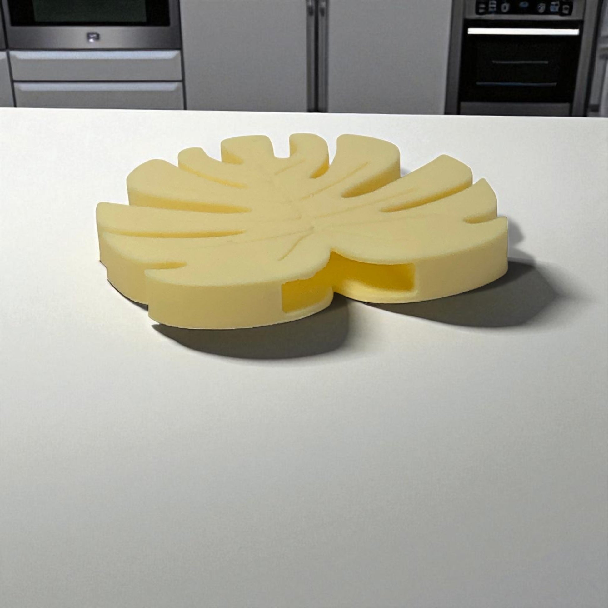 Yellow leaf-shaped object on a white surface with kitchen appliances in the background