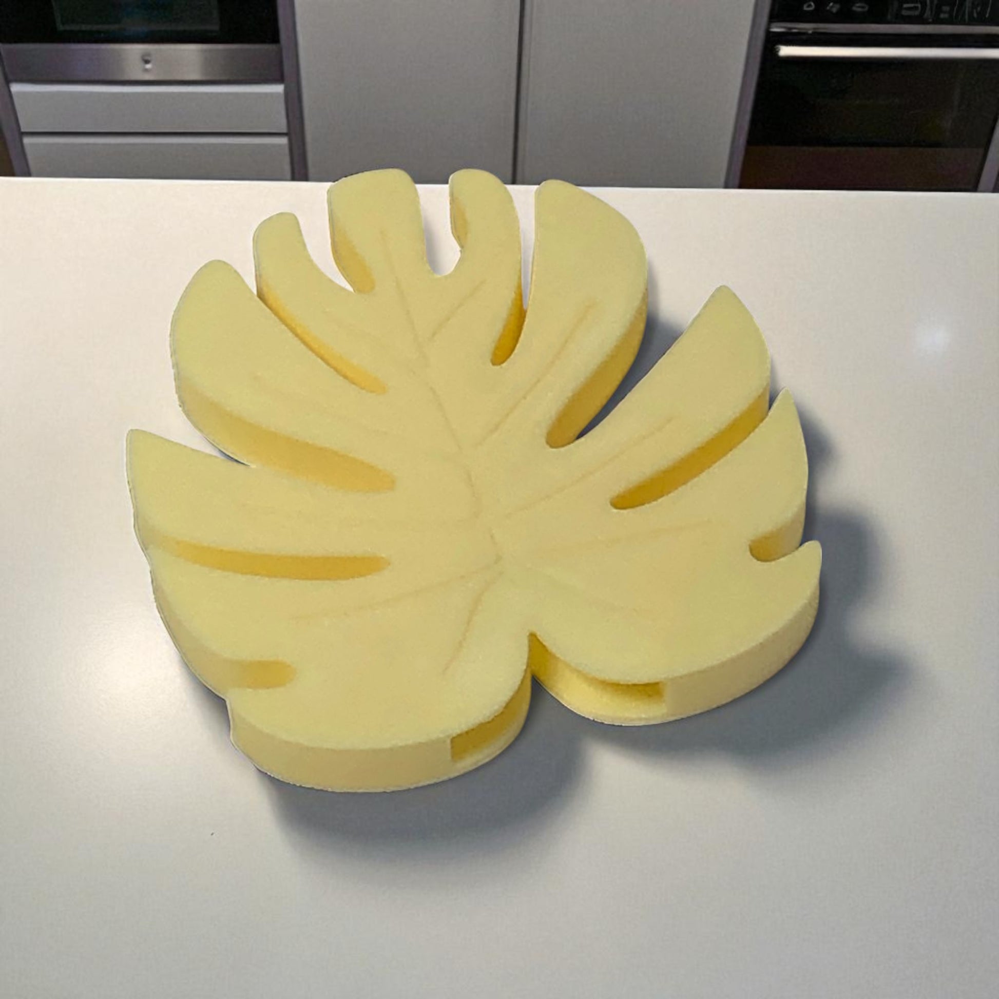 Yellow leaf-shaped object on a white surface with kitchen appliances in the background