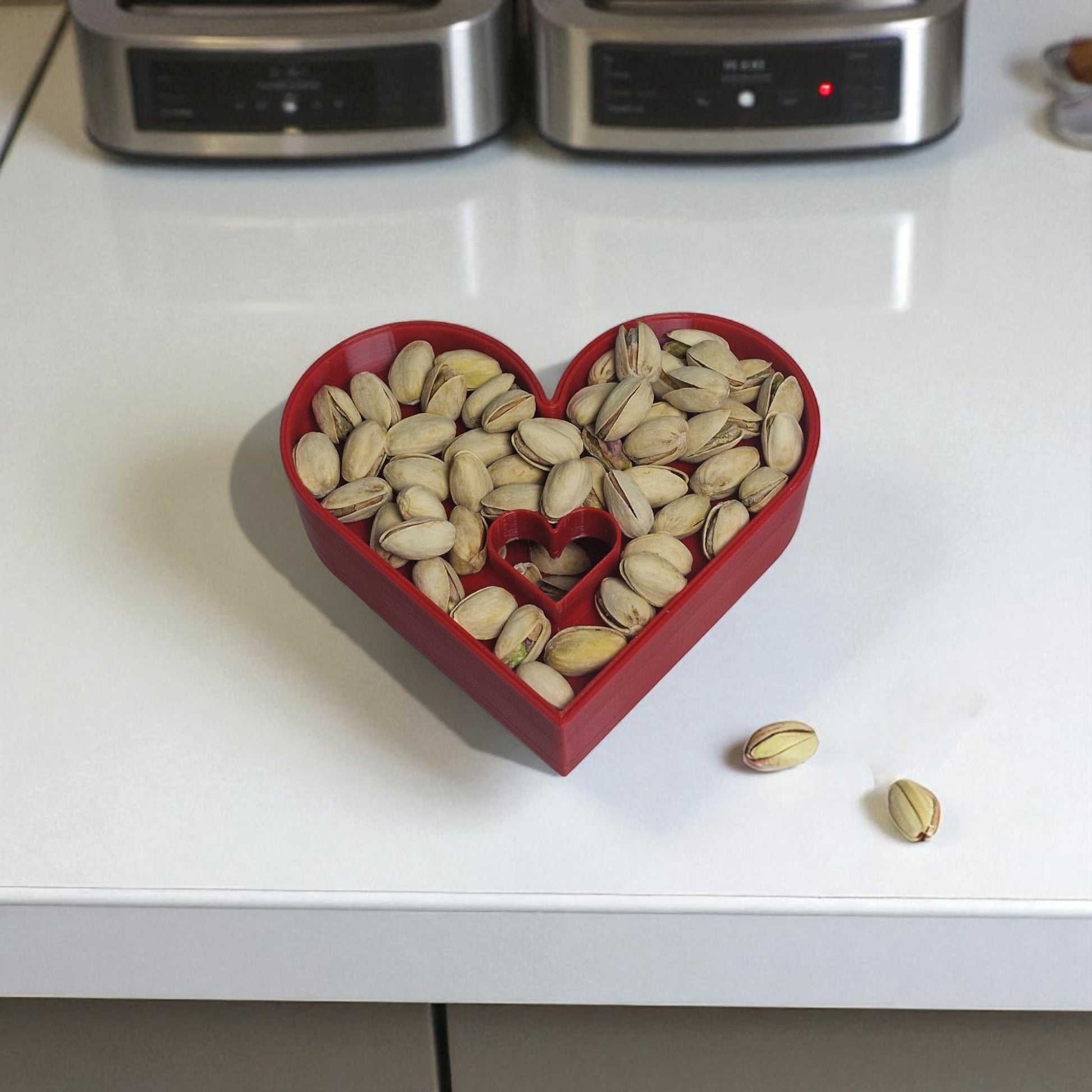 Heart-shaped red container filled with pistachios on a white countertop