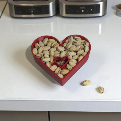 Heart-shaped red container filled with pistachios on a white countertop