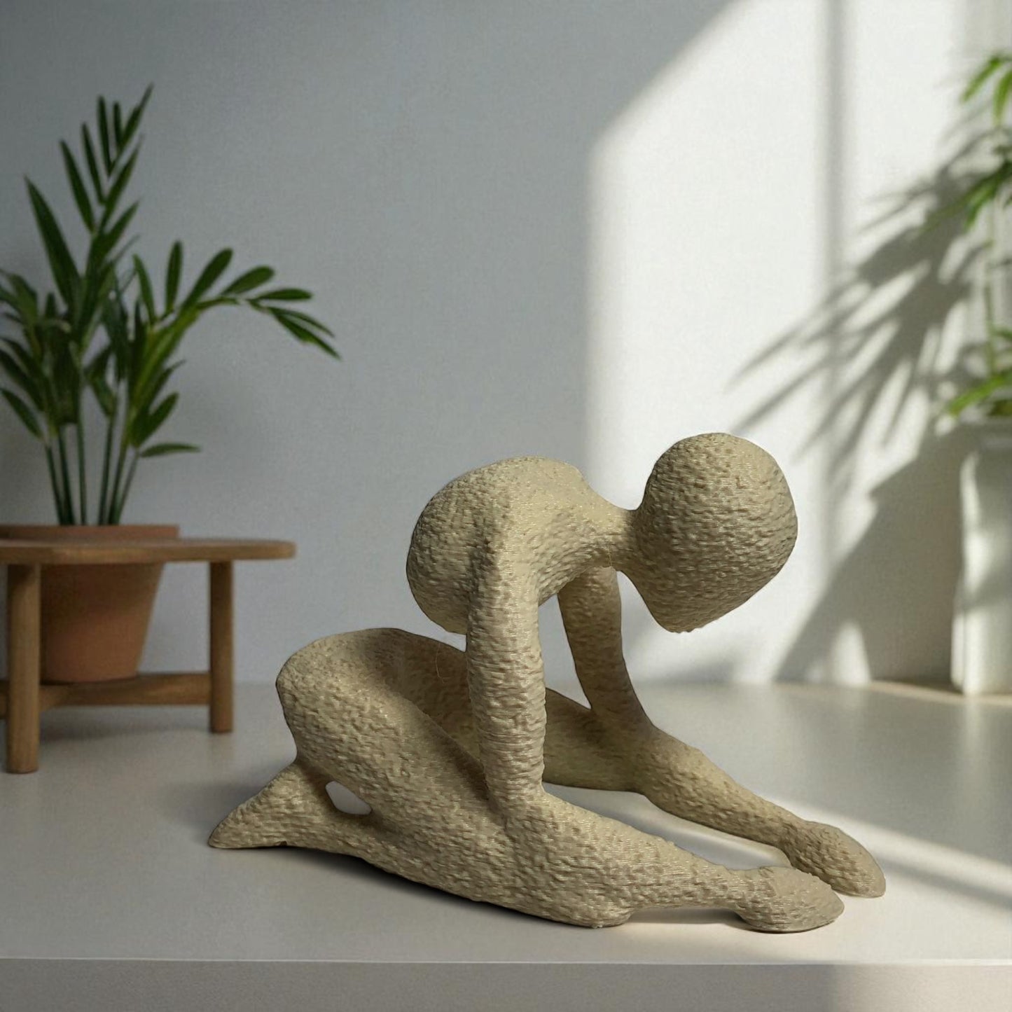 beige abstract sculpture on a white surface with plants in the background