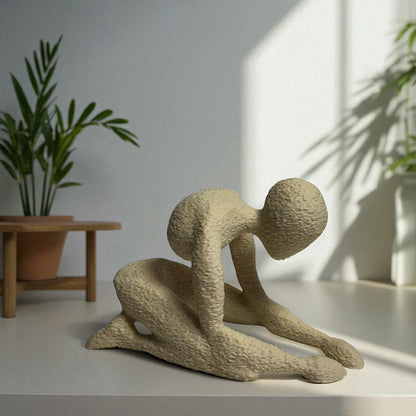 Beige abstract sculpture on a white surface with plants in the background