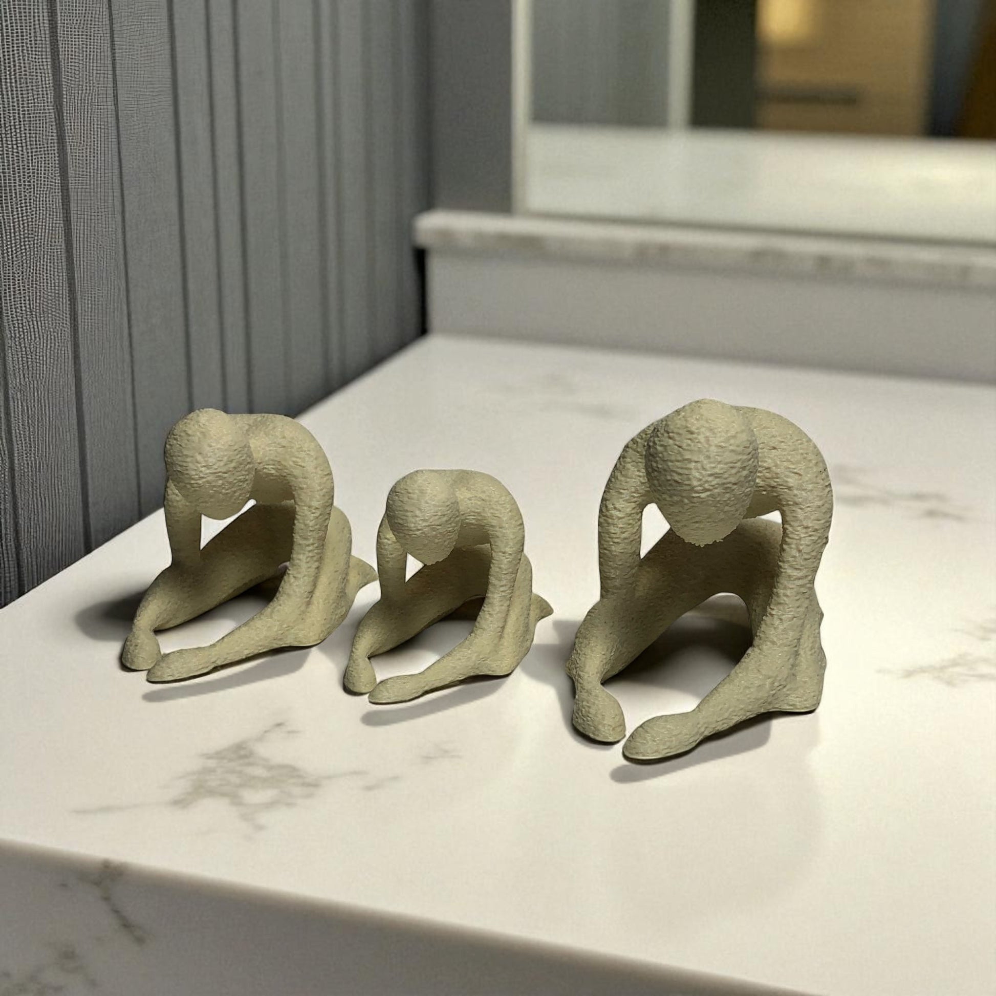 Three beige ceramic figures on a marble surface with a neutral background