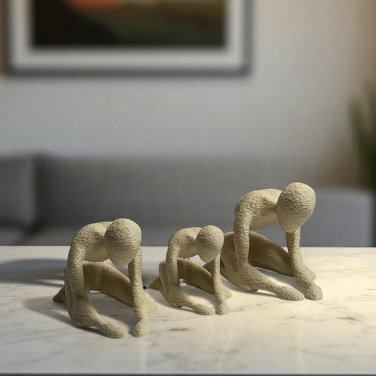Three beige abstract sculptures on a marble surface with a blurred indoor background