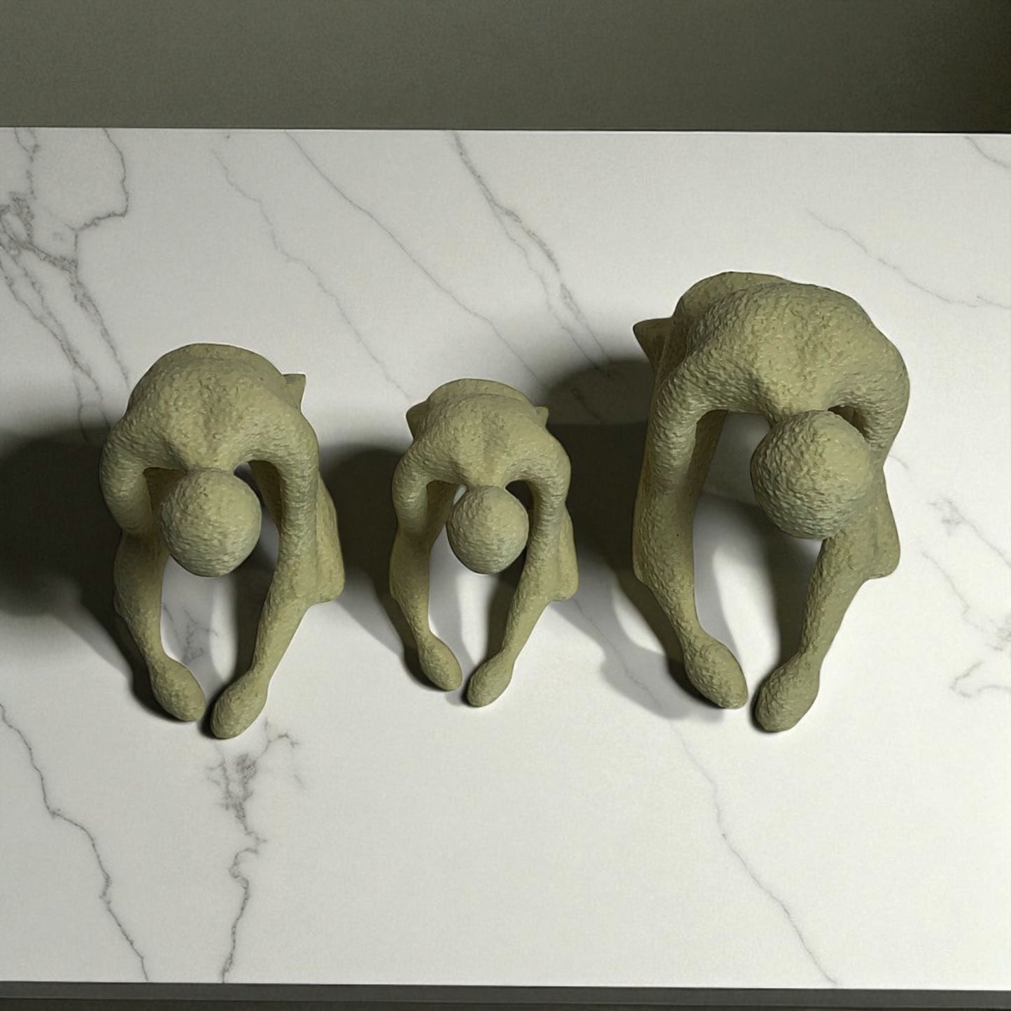 three green ceramic sculptures of people in various poses on a marble surface