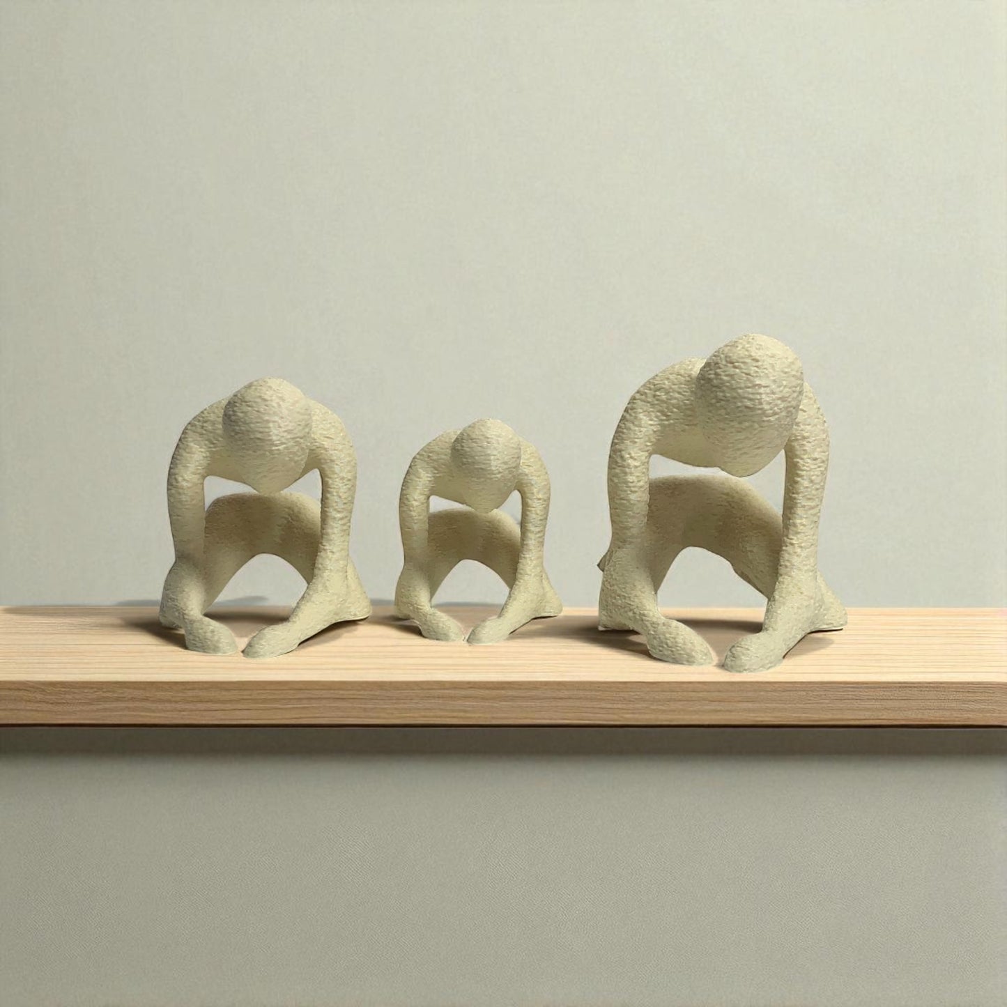 three abstract stone sculptures on a wooden shelf against a plain background