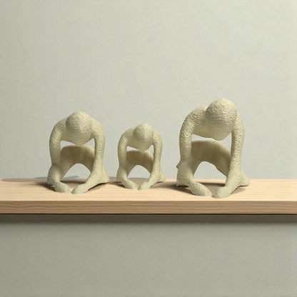 Three abstract stone sculptures on a wooden shelf against a plain background