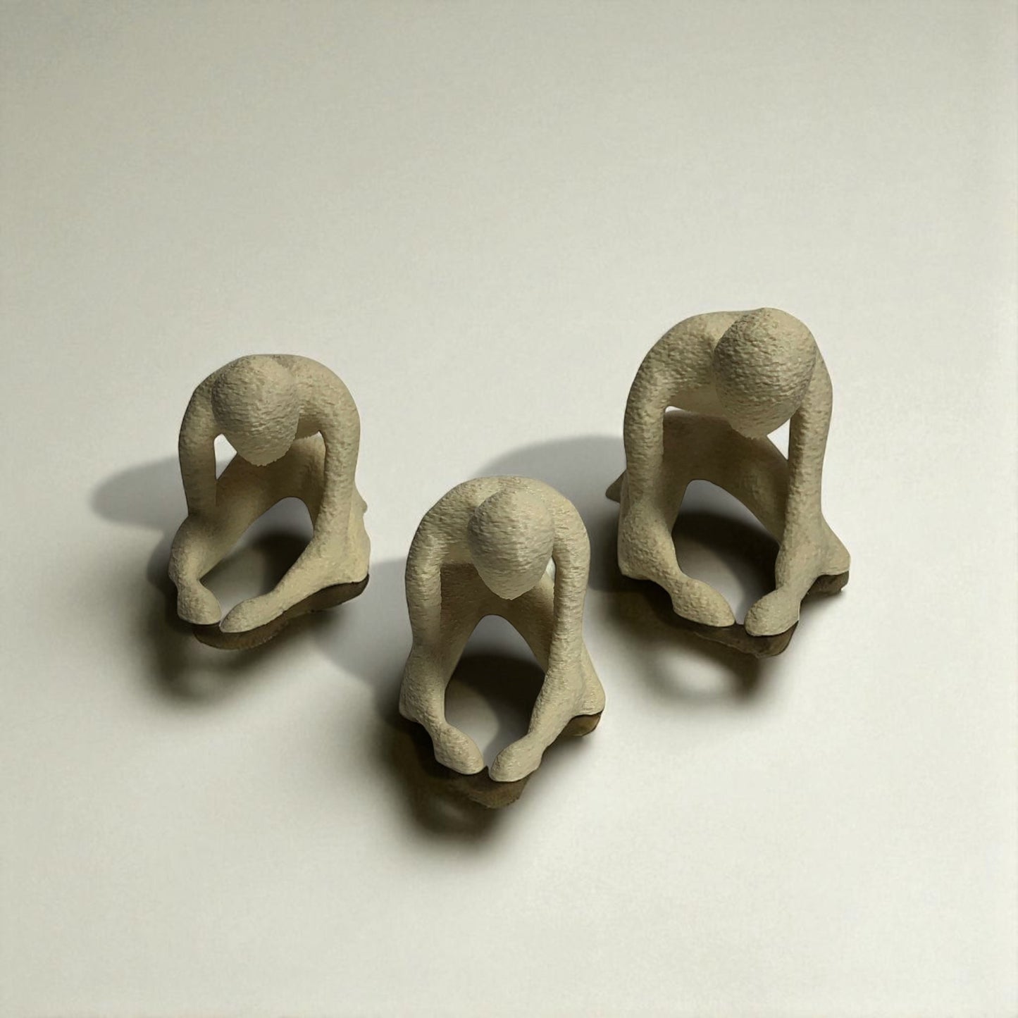 three small beige figurines of people in various poses on a light background