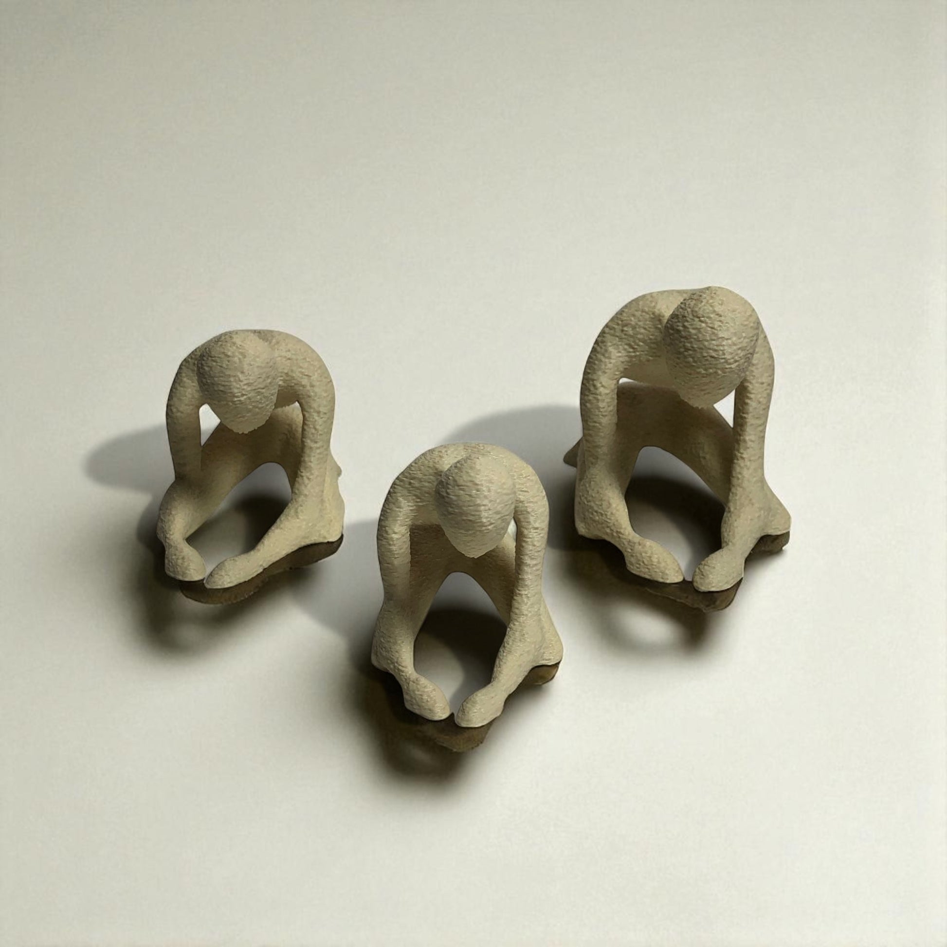 Three small beige figurines of people in various poses on a light background