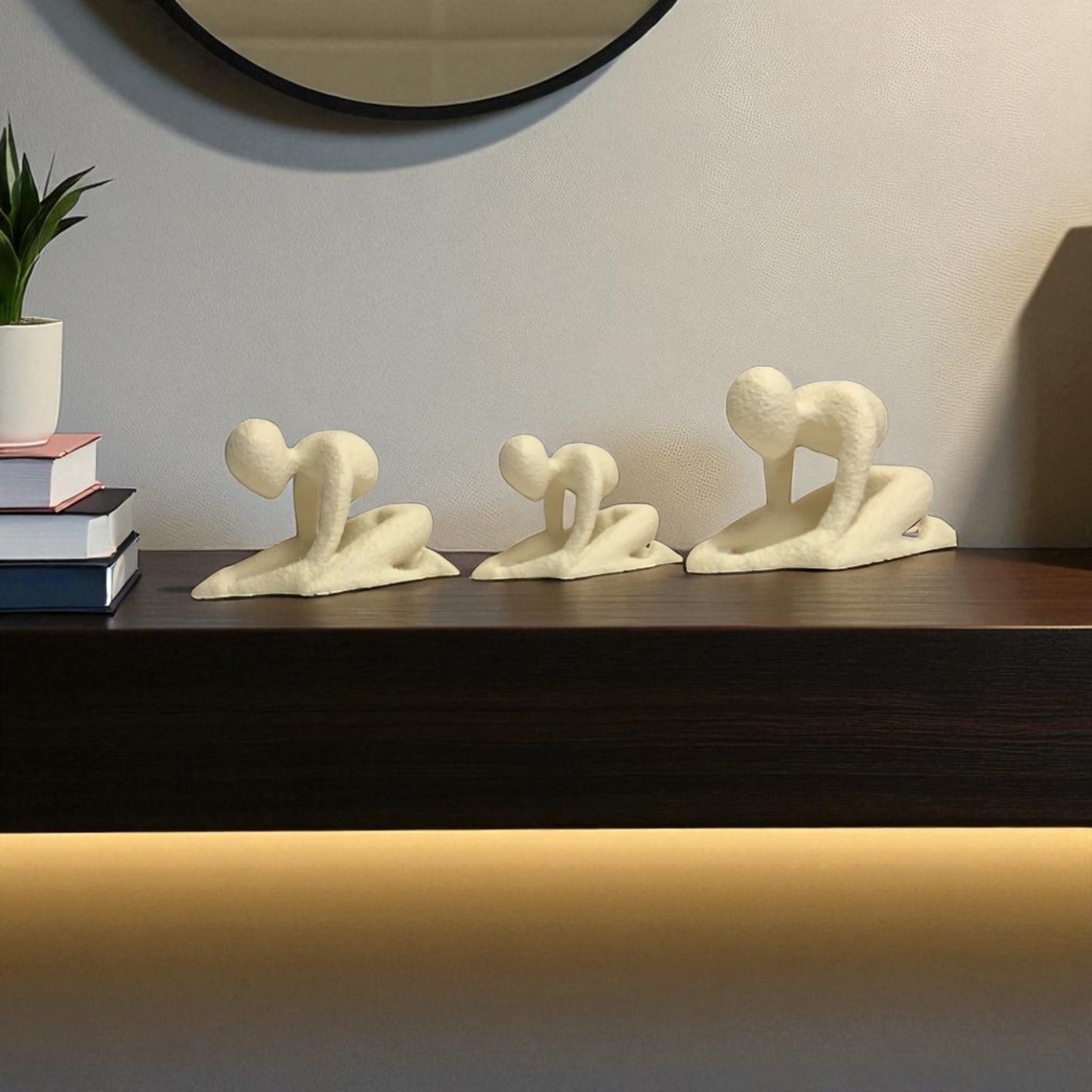 three white abstract sculptures on a dark surface with a light gray wall in the background.