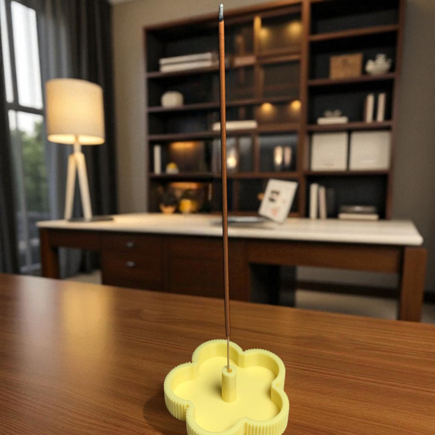 yellow incense burner with a single incense stick on a wooden table in a room with a bookshelf and lamp.
