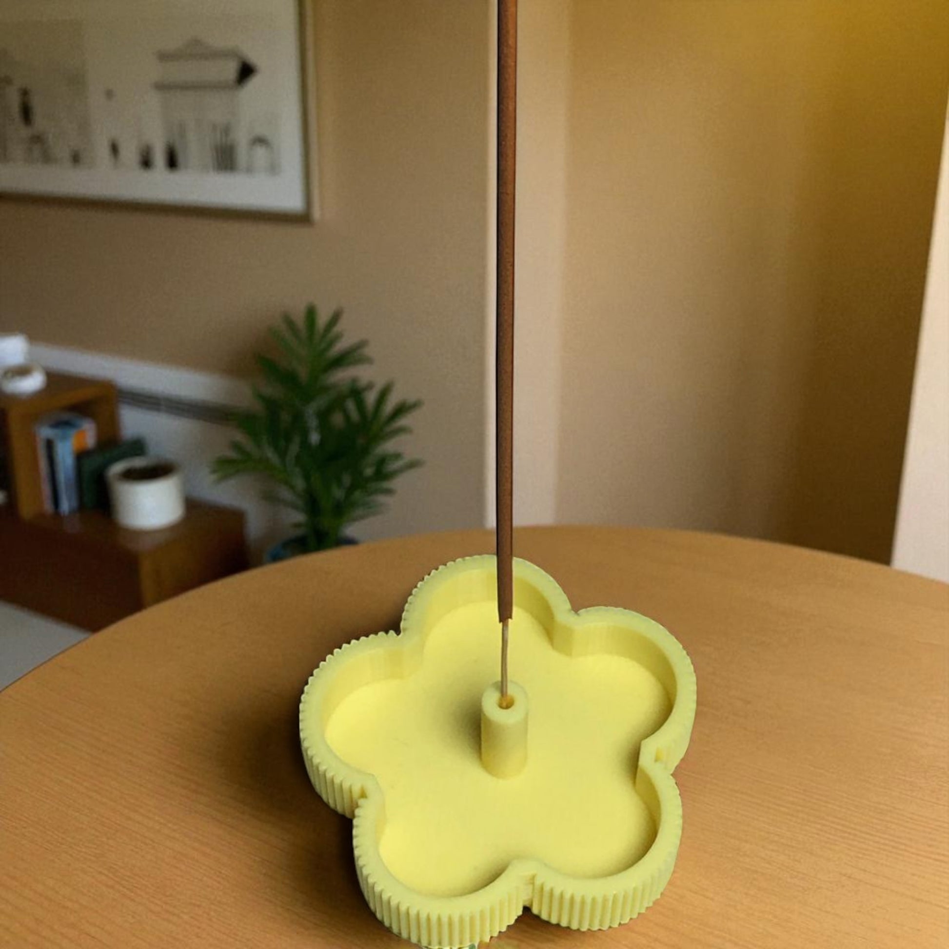 Yellow flower-shaped incense holder on a wooden table with a blurred indoor background