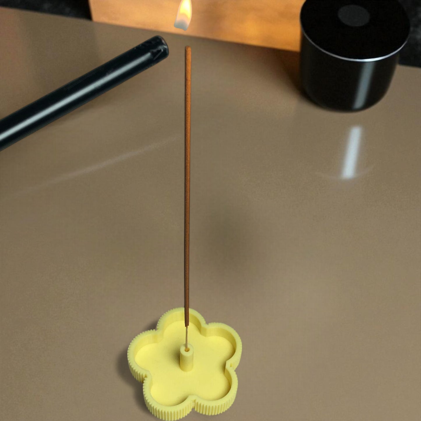 yellow incense holder with a single incense stick on a reflective surface