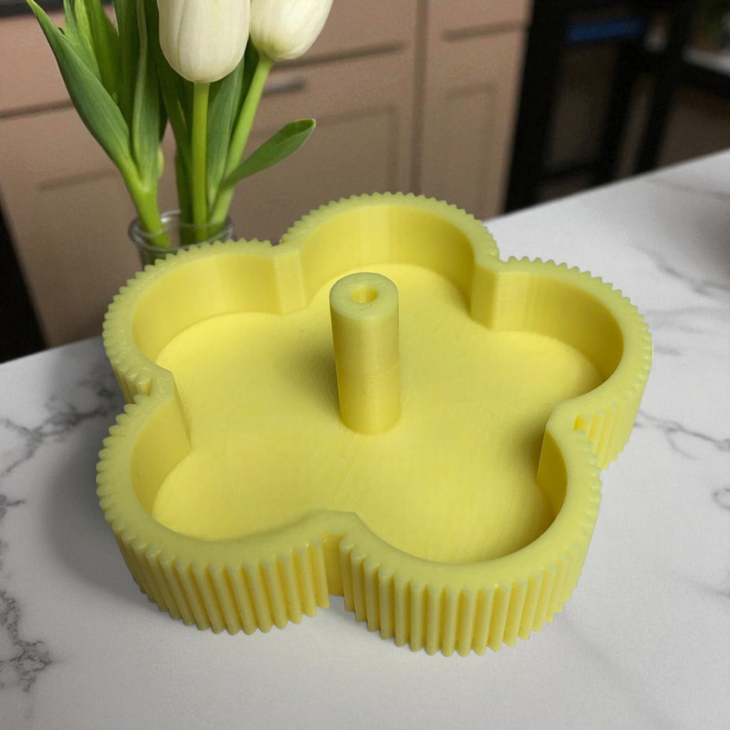 yellow flower-shaped candle mold on a marble surface with white tulips in the background.