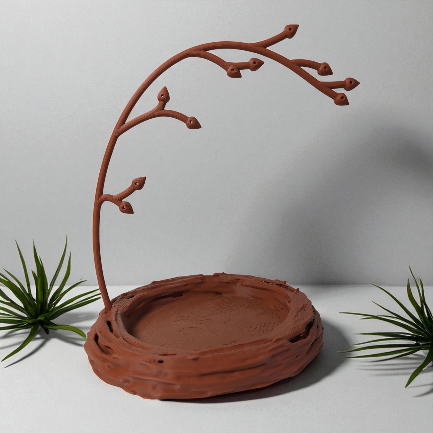a uniquely designed bird nest jewelry tray with a branch, perfect for organizing rings, earrings, necklaces, and bracelets. the nest-shaped base includes small holes for earring storage, while the branch provides an elegant spot for hanging jewelry. made from durable, eco-friendly 3d-printed material, this nature-inspired jewelry organizer adds a stylish and functional touch to any vanity or dresser.