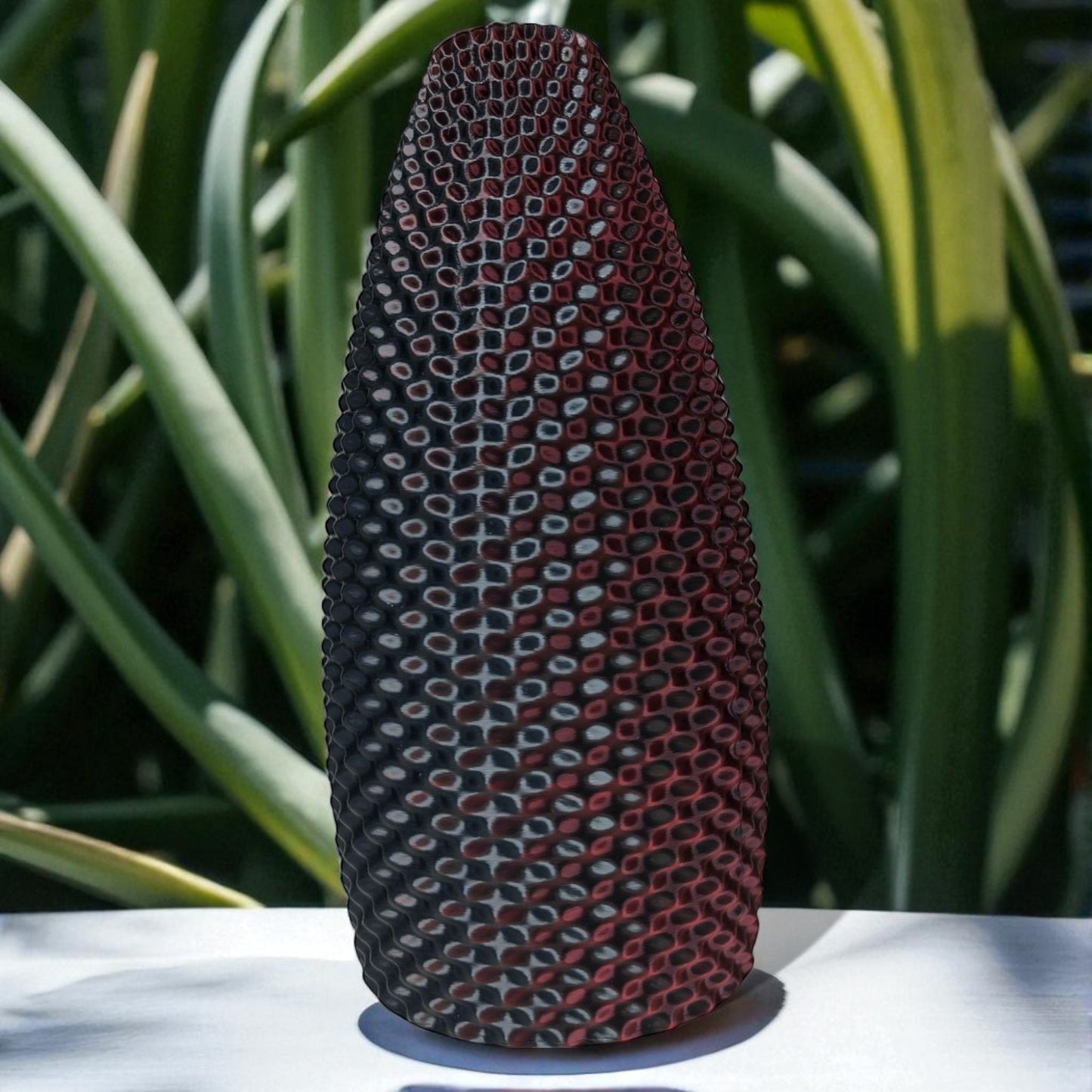 textured vase with geometric pattern on a white surface with green foliage in the background