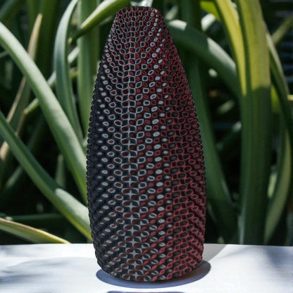 Textured vase with geometric pattern on a white surface with green foliage in the background