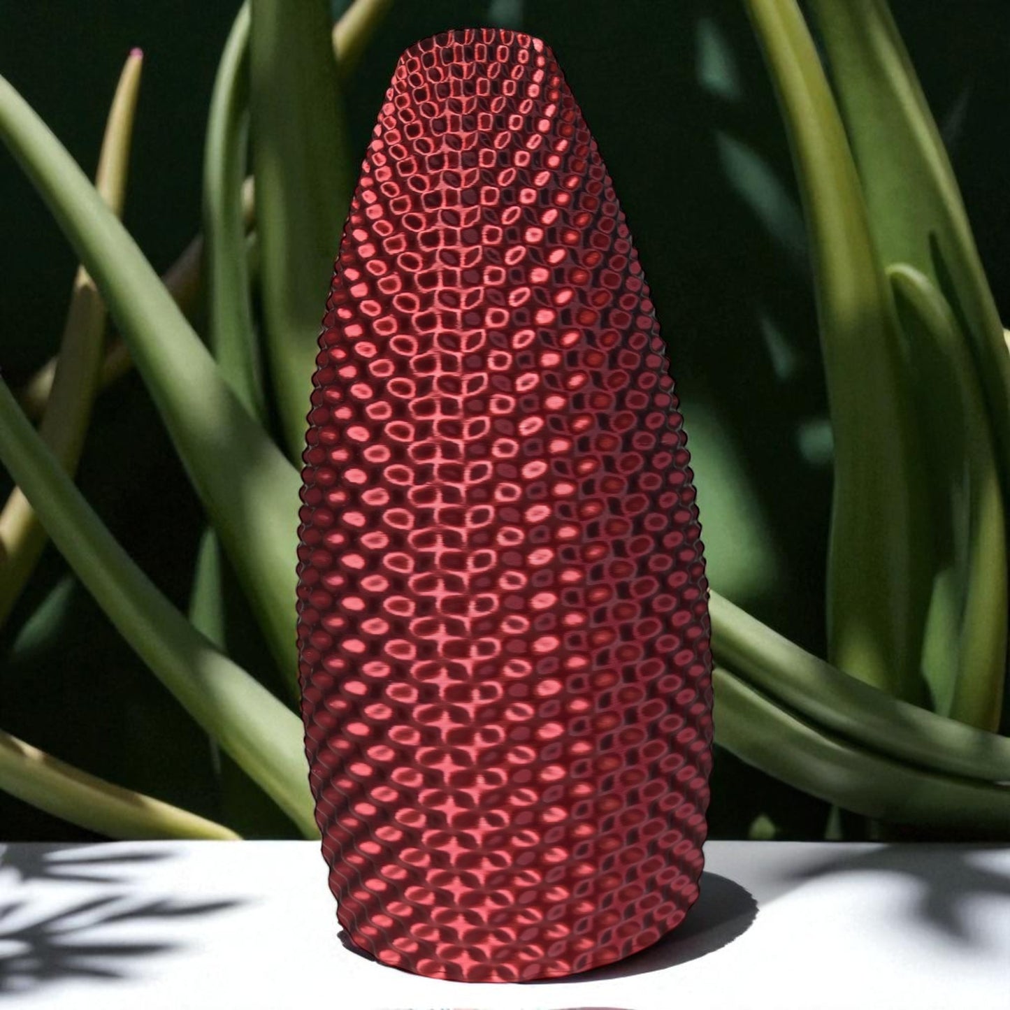 red textured vase with green plants in the background