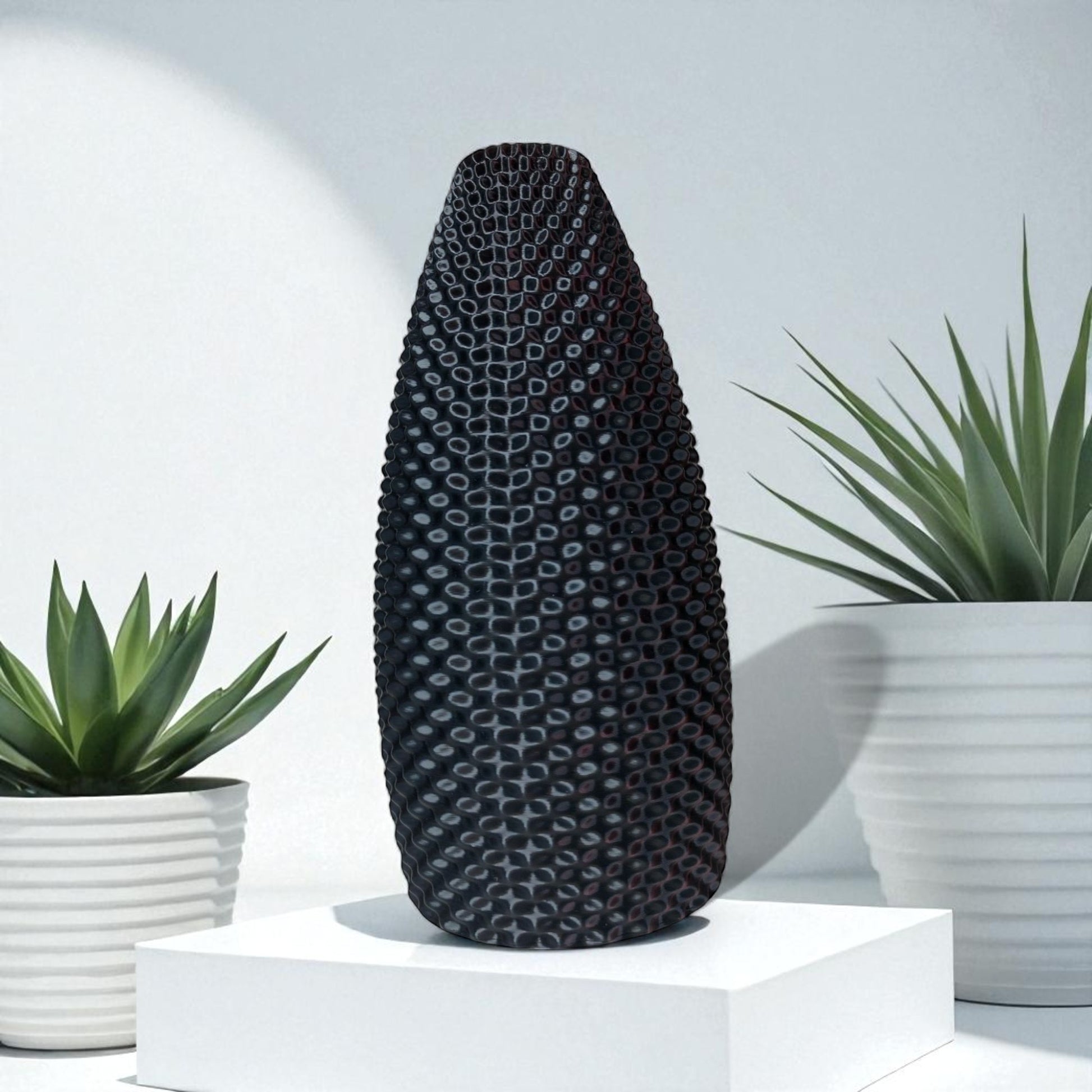 Black textured vase on a white platform with plants in the background