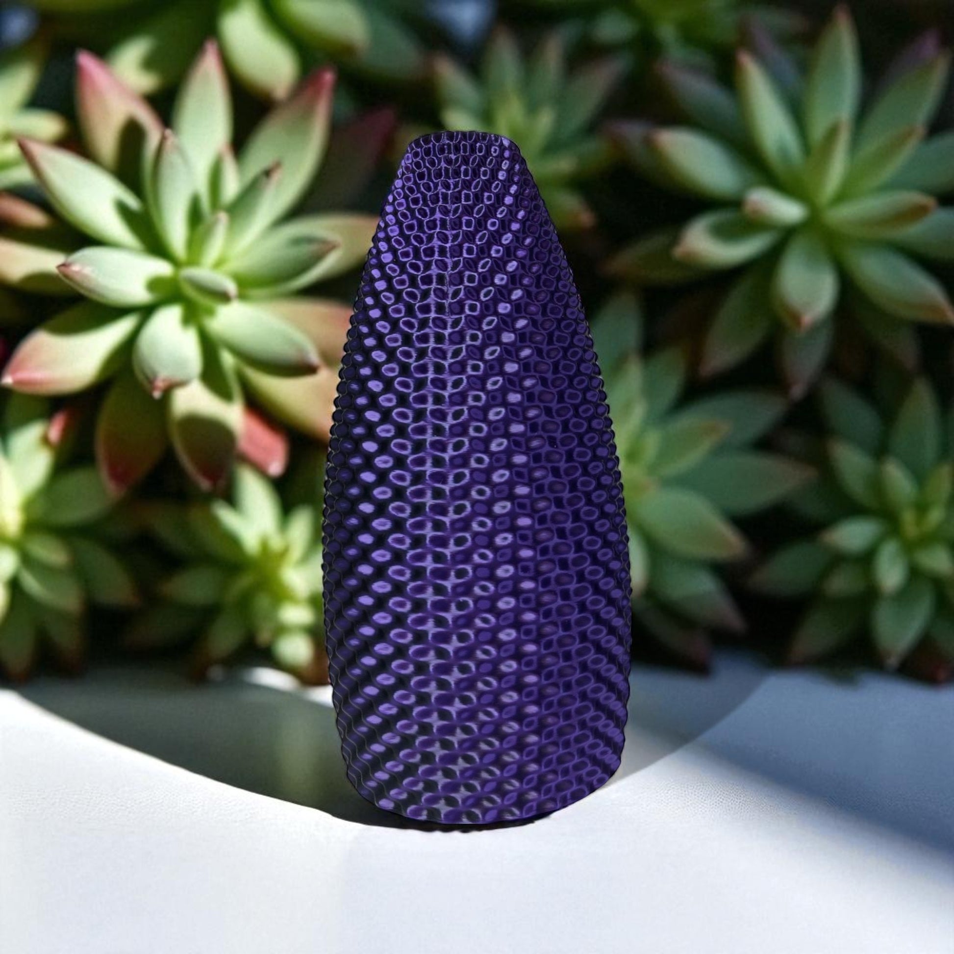 Purple textured object on a white surface with succulents in the background