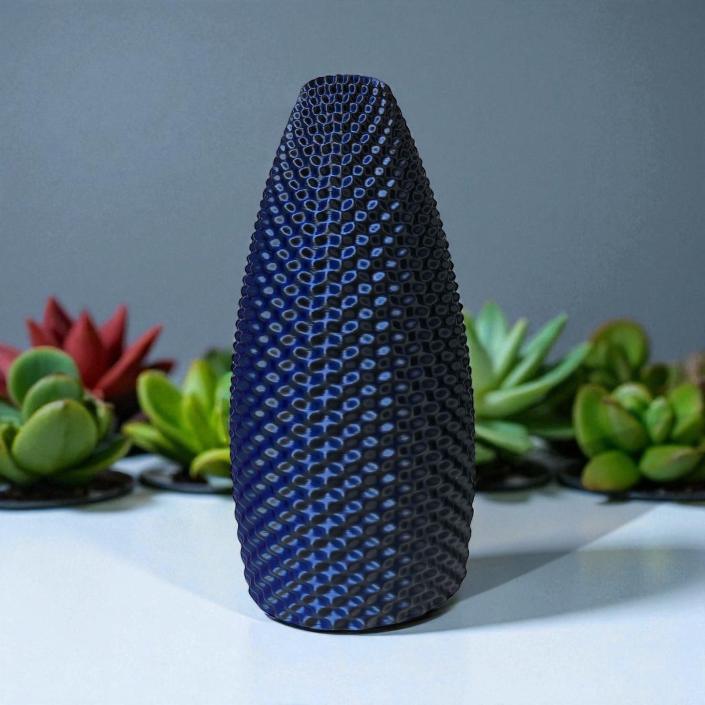 textured blue and black vase on a white surface with plants in the background
