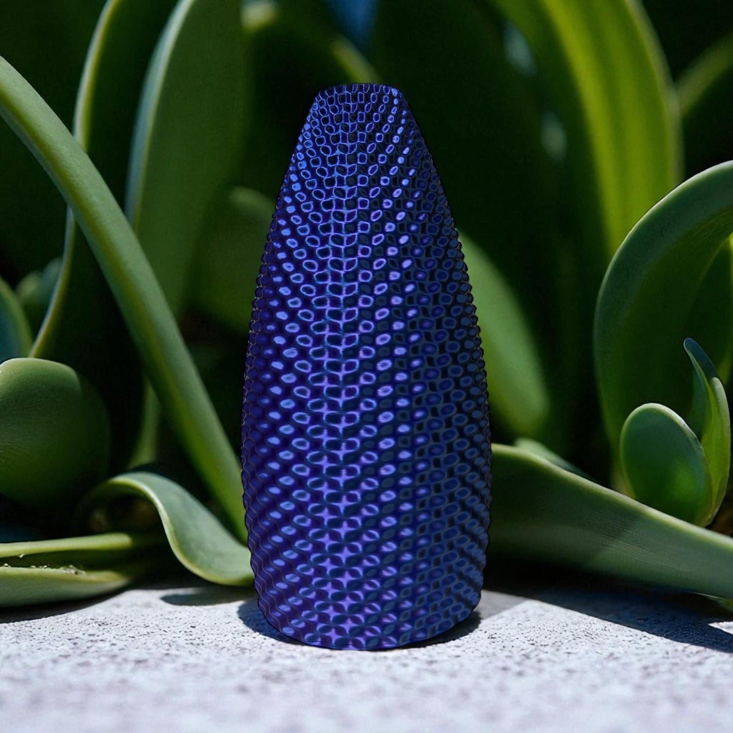 blue textured vase on a concrete surface with green plants in the background