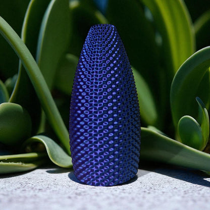 Blue textured vase on a concrete surface with green plants in the background