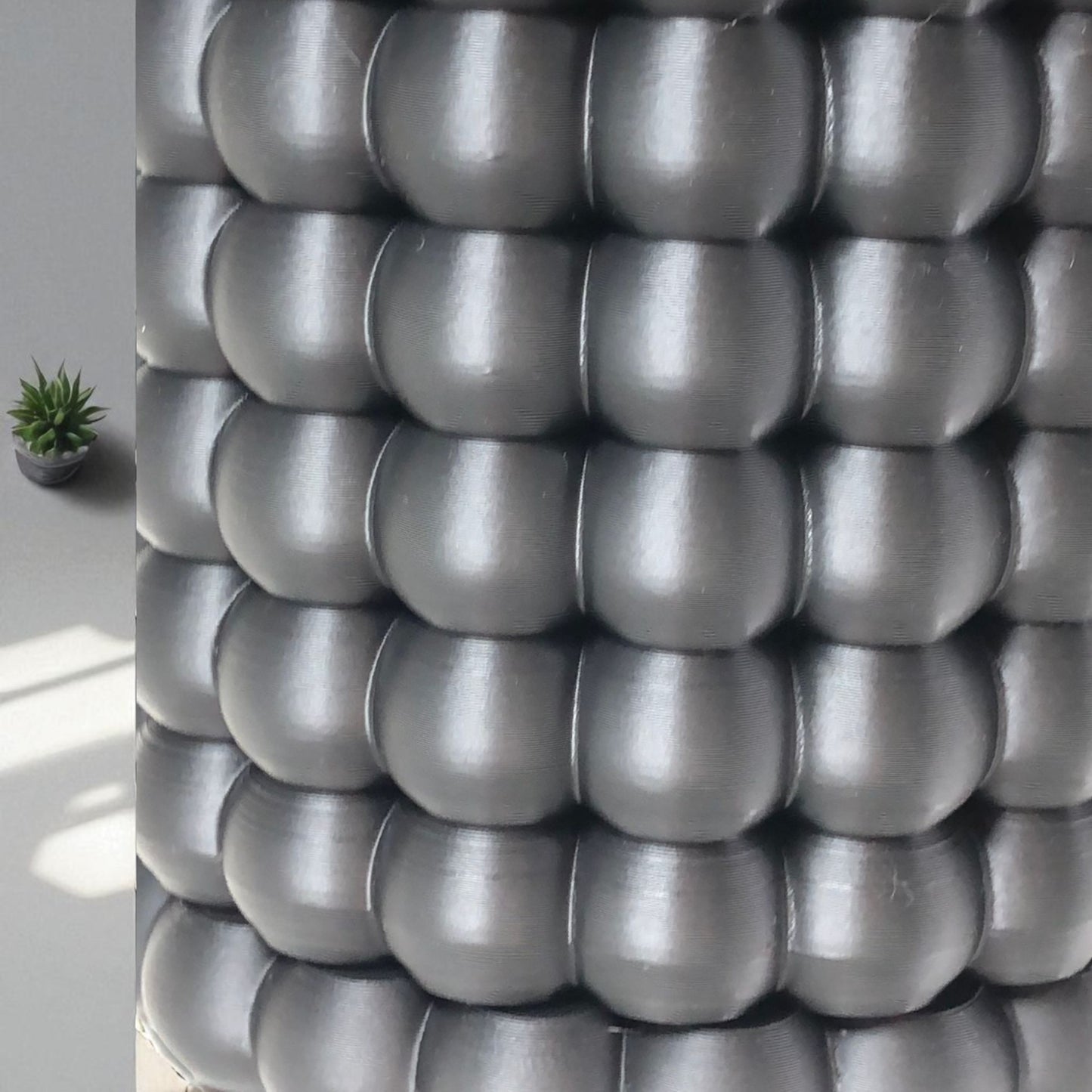 modern black wall-mounted planter with a bubble texture design, holding a green succulent plant. includes mounting bracket for screws or adhesive and a built-in water tray.