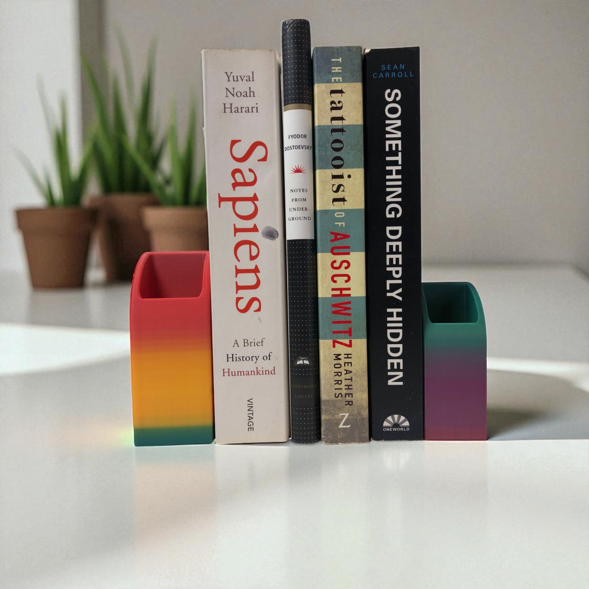 Colorful 3D printed rainbow-shaped organizer used as a bookend, pen holder, and mini vase, displayed in two sizes on a shelf with books, stationery, and dried flowers.