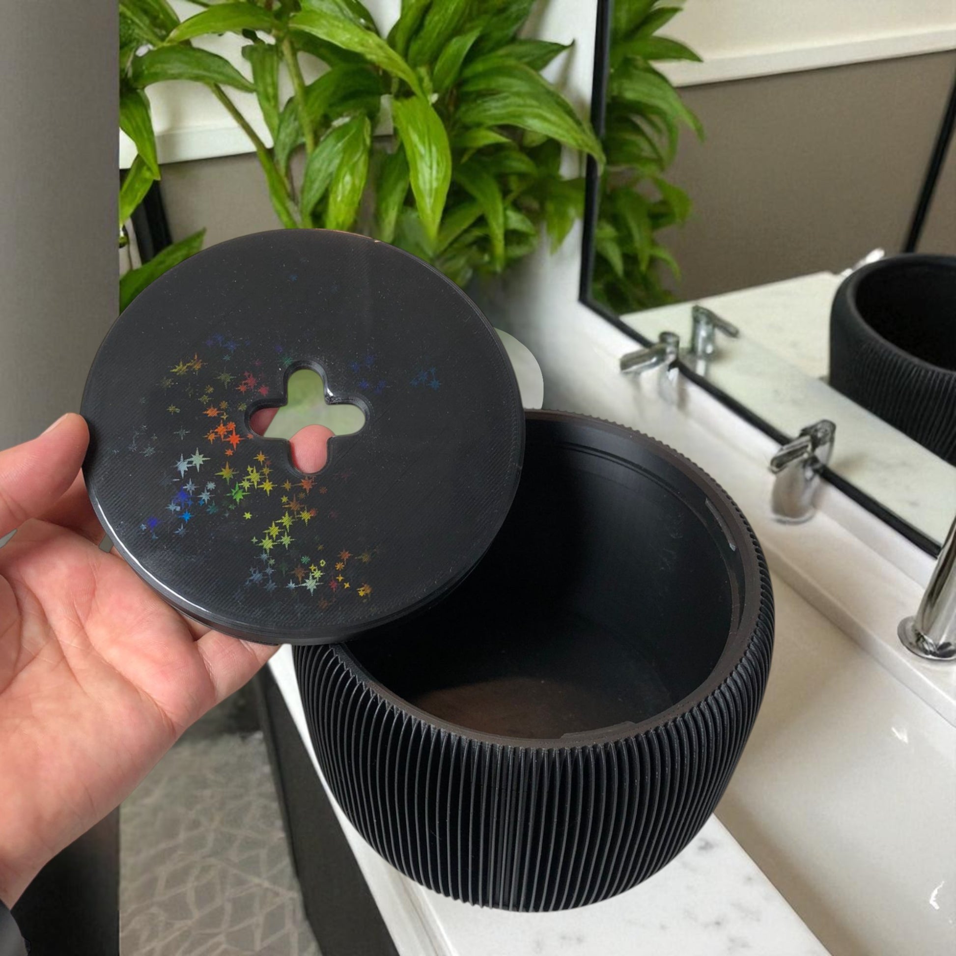 Modern black toilet paper holder with ribbed texture and lid, designed to prevent pets or children from unrolling the paper. Stylish and compact bathroom accessory shown on a white surface.