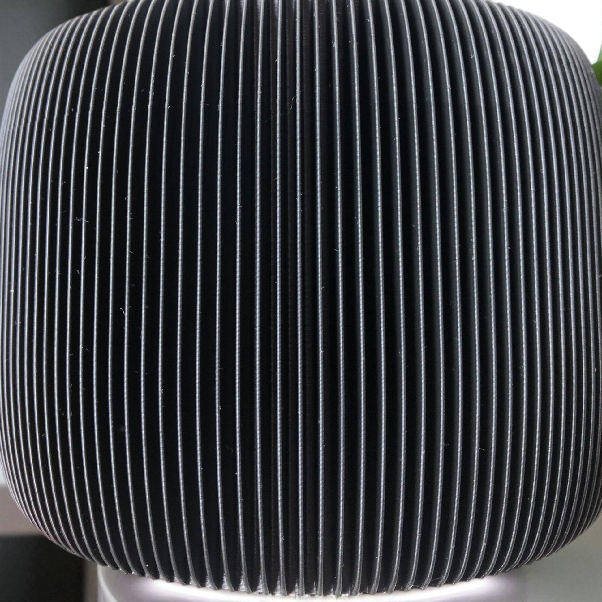 Modern black toilet paper holder with ribbed texture and lid, designed to prevent pets or children from unrolling the paper. Stylish and compact bathroom accessory shown on a white surface.