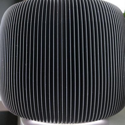 Modern black toilet paper holder with ribbed texture and lid, designed to prevent pets or children from unrolling the paper. Stylish and compact bathroom accessory shown on a white surface.