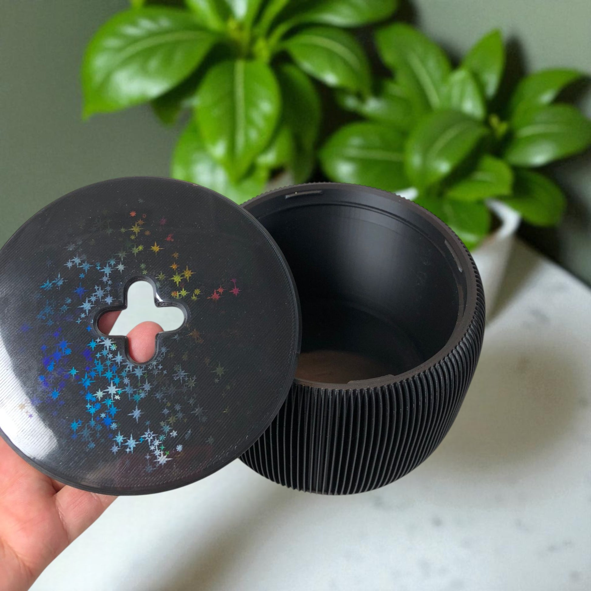 Modern black toilet paper holder with ribbed texture and lid, designed to prevent pets or children from unrolling the paper. Stylish and compact bathroom accessory shown on a white surface.