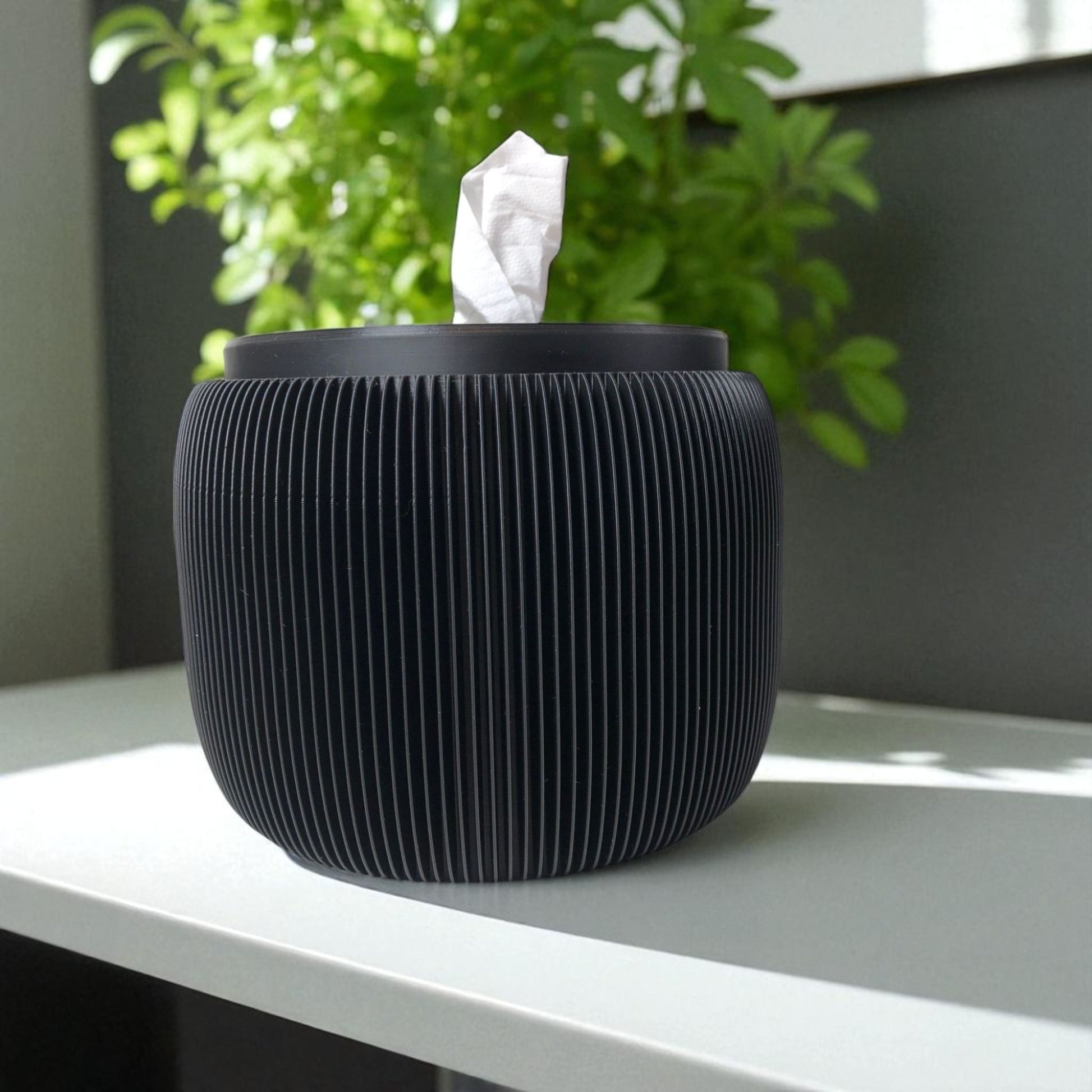 Modern black toilet paper holder with ribbed texture and lid, designed to prevent pets or children from unrolling the paper. Stylish and compact bathroom accessory shown on a white surface.