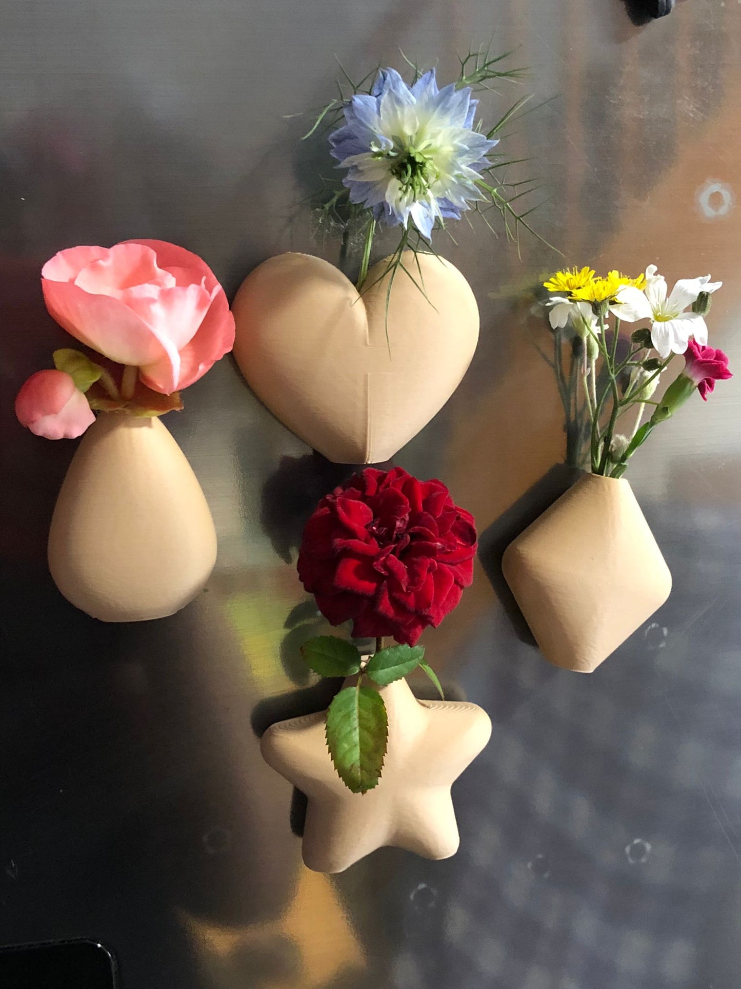 set of mini magnetic vases in heart, star, diamond, and teardrop shapes, attached to a refrigerator and holding small colorful flowers, displayed in red and white colors.