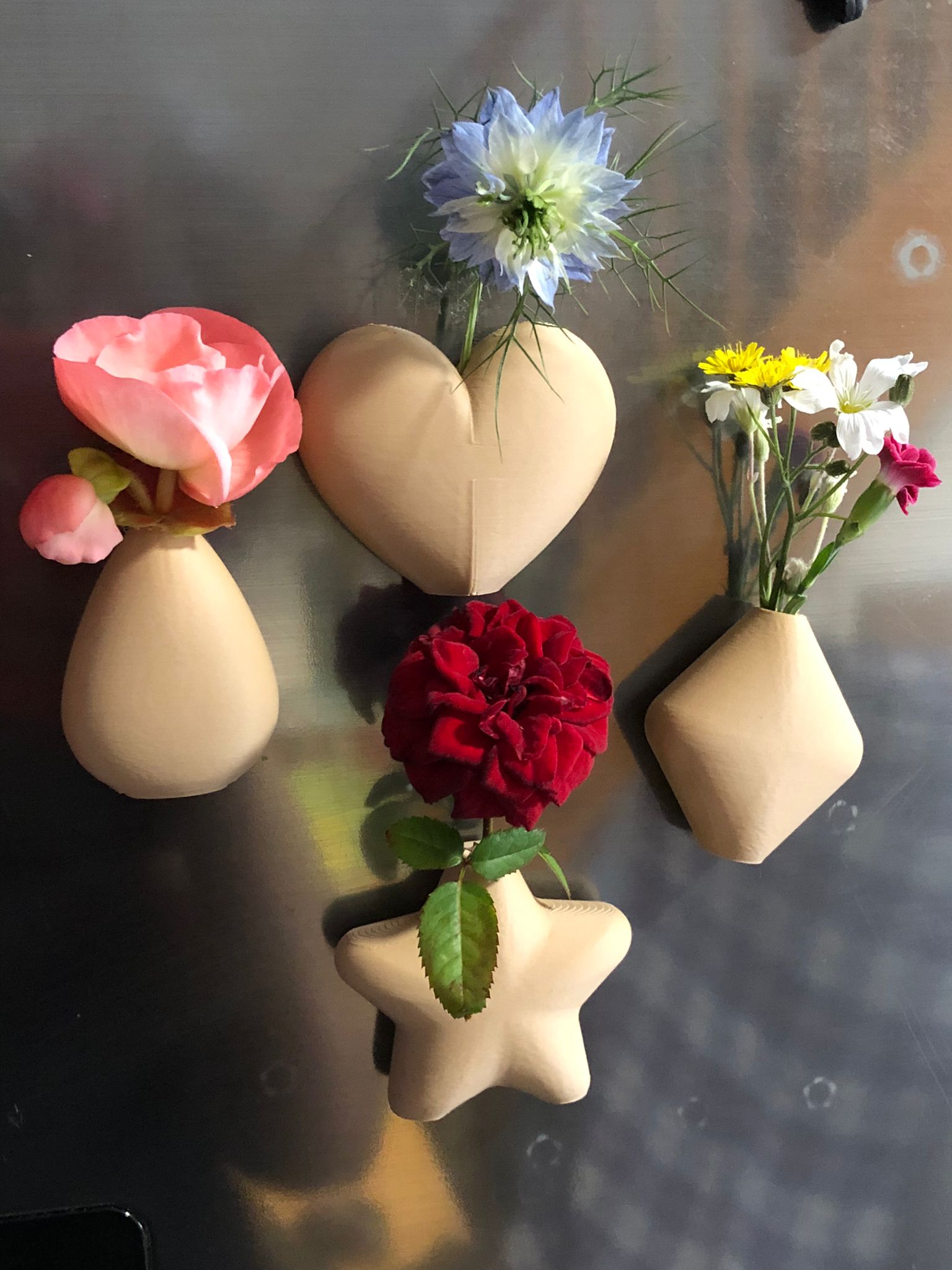 Set of mini magnetic vases in heart, star, diamond, and teardrop shapes, attached to a refrigerator and holding small colorful flowers, displayed in red and white colors.