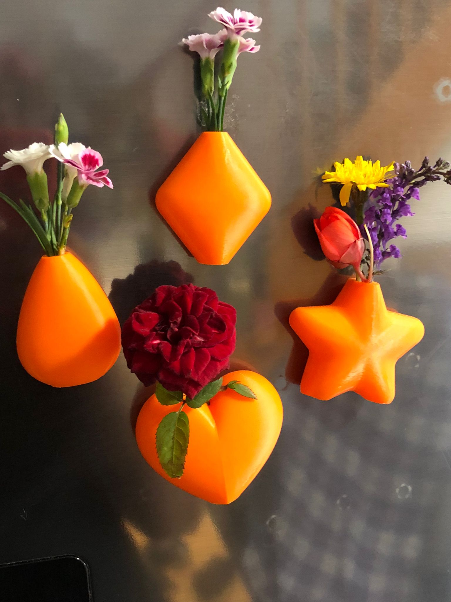 Set of mini magnetic vases in heart, star, diamond, and teardrop shapes, attached to a refrigerator and holding small colorful flowers, displayed in red and white colors.