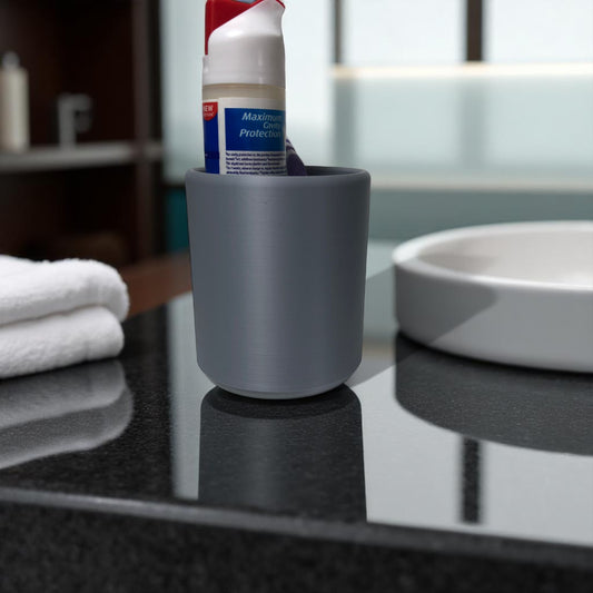 Modern minimalist toothbrush cup and soap dish set, 3D printed and available in multiple colours including grey, white, charcoal, and beige. Toothbrush holder shown with toothpaste and toothbrush inside, and soap tray holding a white bar of soap. Designed for stylish and organized bathroom use.