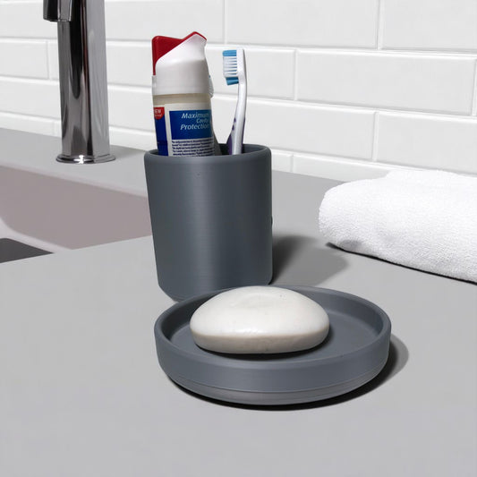 Modern minimalist toothbrush cup and soap dish set, 3D printed and available in multiple colours including grey, white, charcoal, and beige. Toothbrush holder shown with toothpaste and toothbrush inside, and soap tray holding a white bar of soap. Designed for stylish and organized bathroom use.